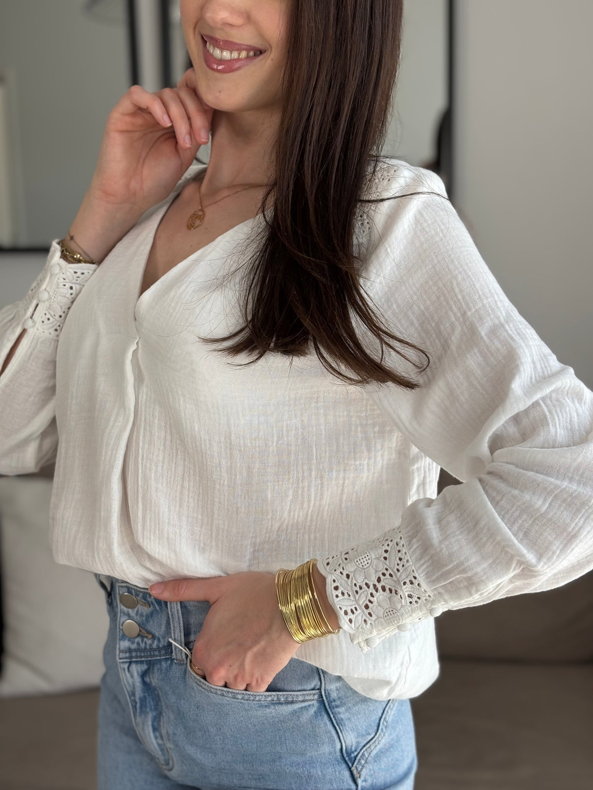 Délicate blouse Solène en gaze de coton écru, ornée de broderies élégantes aux épaules et aux manches. Son col V et ses manches longues apportent une touche de féminité intemporelle. Confectionnée en 100% coton, elle allie légèreté et confort pour sublimer votre silhouette avec raffinement.