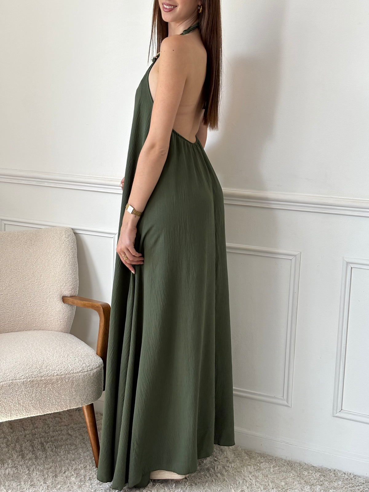 Adoptez une allure audacieuse avec cette robe longue kaki Adeje. Son col montant réglable, orné d’un détail doré, apporte une touche sophistiquée tandis que l’élastique au dos assure un confort parfait. Sans manches et à la coupe ample, elle offre une liberté de mouvement idéale pour affirmer votre style avec assurance.&nbsp;