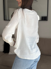 Délicate blouse Solène en gaze de coton écru, ornée de broderies élégantes aux épaules et aux manches. Son col V et ses manches longues apportent une touche de féminité intemporelle. Confectionnée en 100% coton, elle allie légèreté et confort pour sublimer votre silhouette avec raffinement.