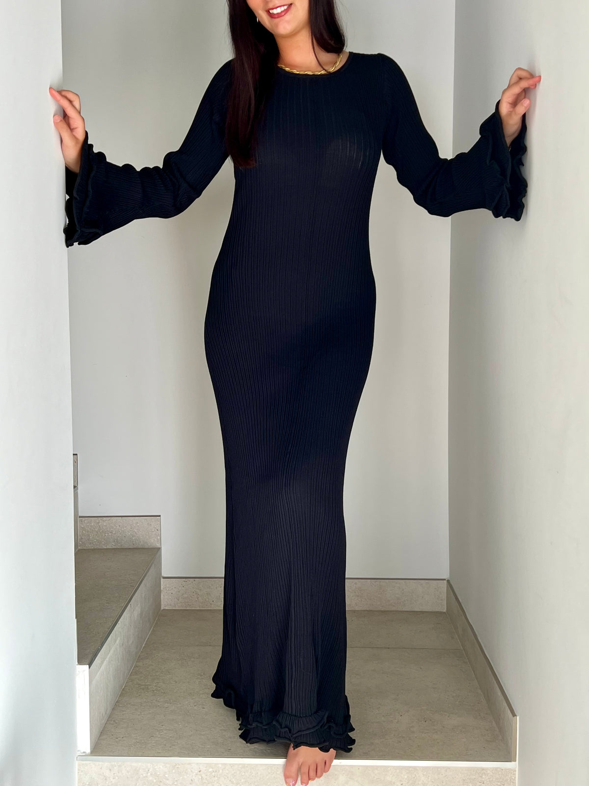 La robe longue noir Esther est un mariage parfait de chic et de confort. Avec ses manches longues et son col rond, elle assure une élégance intemporelle. Mais le dos nu avec lacets croisés et les volants aux manches et au bas de la robe ajoutent une touche ludique et originale. Soyez prête à faire tourner les têtes avec cette robe unique !