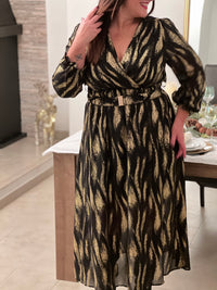 Robe festive Laina, l'allure sophistiquée pour vos soirées. Cette création élégante allie le noir profond et les touches dorées pour une présence rayonnante. Le col cache-cœur flatteuse épouse votre silhouette tandis que la taille élastique offre un confort optimal.
