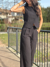 Le gilet de tailleur noir Leonie est la pièce parfaite pour compléter votre tenue formelle avec une touche de chic. Avec son design court et sans manches, ses boutons sur la longueur et son effet croisé sur le bas, il ajoute une sophistication à toute tenue. De plus, il est entièrement doublé pour un confort et une élégance optimaux. (Avec le gilet Leonie, vous serez la définition du style décontracté mais chic !)