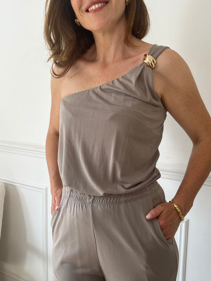 Ce top taupe asymétrique Magaly se distingue par sa coupe moderne et élégante. Sa seule bretelle, non réglable, est sublimée par un détail doré qui apporte une touche raffinée. Le col élastique assure un maintien confortable tout en facilitant l’enfilage. Parfait pour allier style et aisance au quotidien.