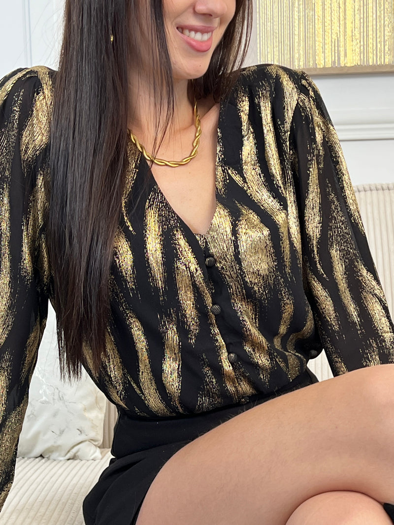 Découvrez la chemise Laina, une pièce festive qui allie élégance et confort. Avec son col V plongeant et ses manches longues ornées de volants délicats, elle crée une silhouette flatteuse et sophistiquée.