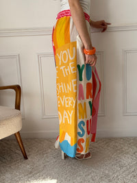 Ce pantalon en lin aux motifs colorés et inspirés des vacances respire la bonne humeur. Avec ses inscriptions comme "You are my Sunshine", "Lemoncello" ou "You are the Sunshine in everyday", il invite à la détente et à l’évasion. Ses teintes de beige, vert, orange, rose, rouge et bleu en font une pièce pétillante, idéale pour un look estival plein de charme et de légèreté.