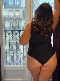 Body noir grande taille conçu pour sublimer votre silhouette avec élégance. Coupe sans manches et col V qui affine la ligne, agrémentée de légers plis latéraux pour un confort optimal. Fermeture par attache crochets pratique et discrète. Pièce incontournable en noir pur, parfaite pour créer des looks épurés et intemporels.