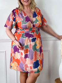 La robe courte Olympe est parfaite pour les femmes aux formes généreuses. Avec ses motifs colorés, elle apporte de la joie et de la vitalité à votre look. Les manches courtes et le col V mettent en valeur votre silhouette. La taille élastique au dos assure un confort optimal. Disponible en bleu, orange, écru, rose, violet, jaune et vert. La jupe est doublée pour un tomber parfait et la matière fine est agréable à porter. Ajoutez de la couleur à votre garde-robe avec la robe Olympe !
