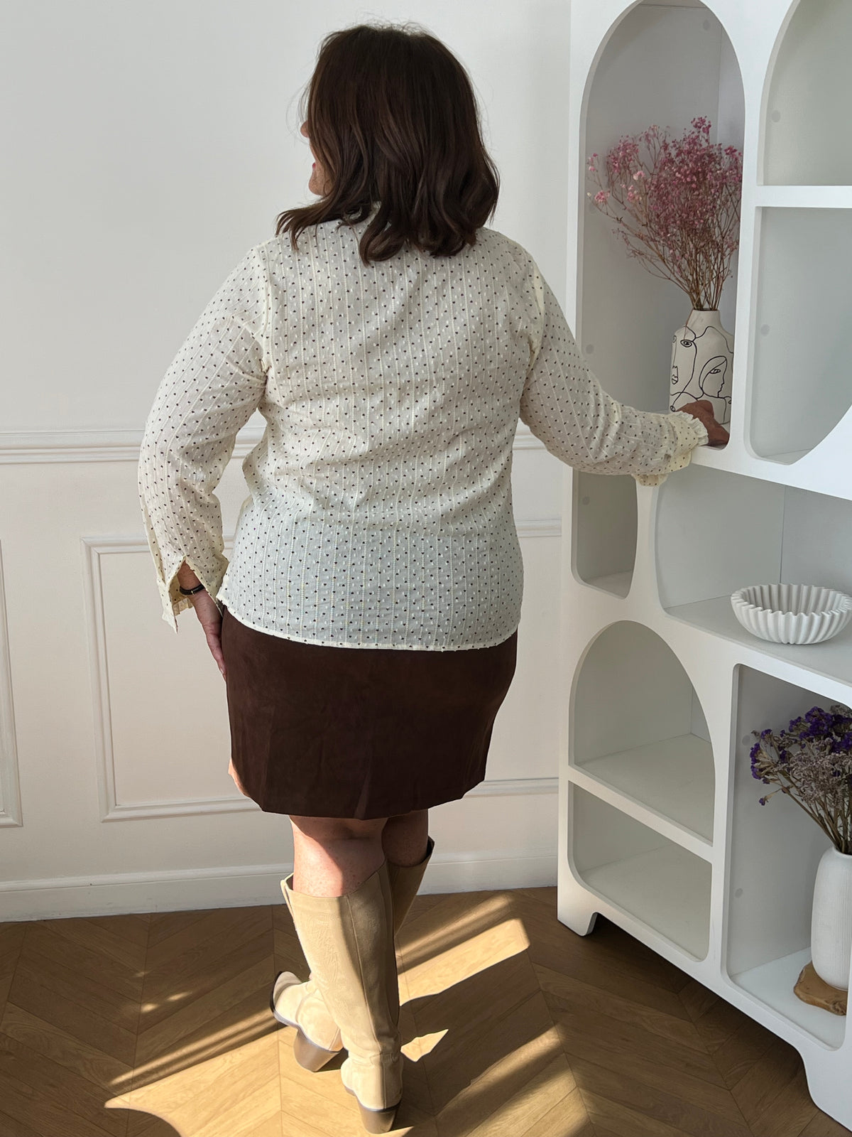 Chemise beige Sofia portée de dos, montrant les petits motifs foncés et les manches longues, avec une jupe marron.