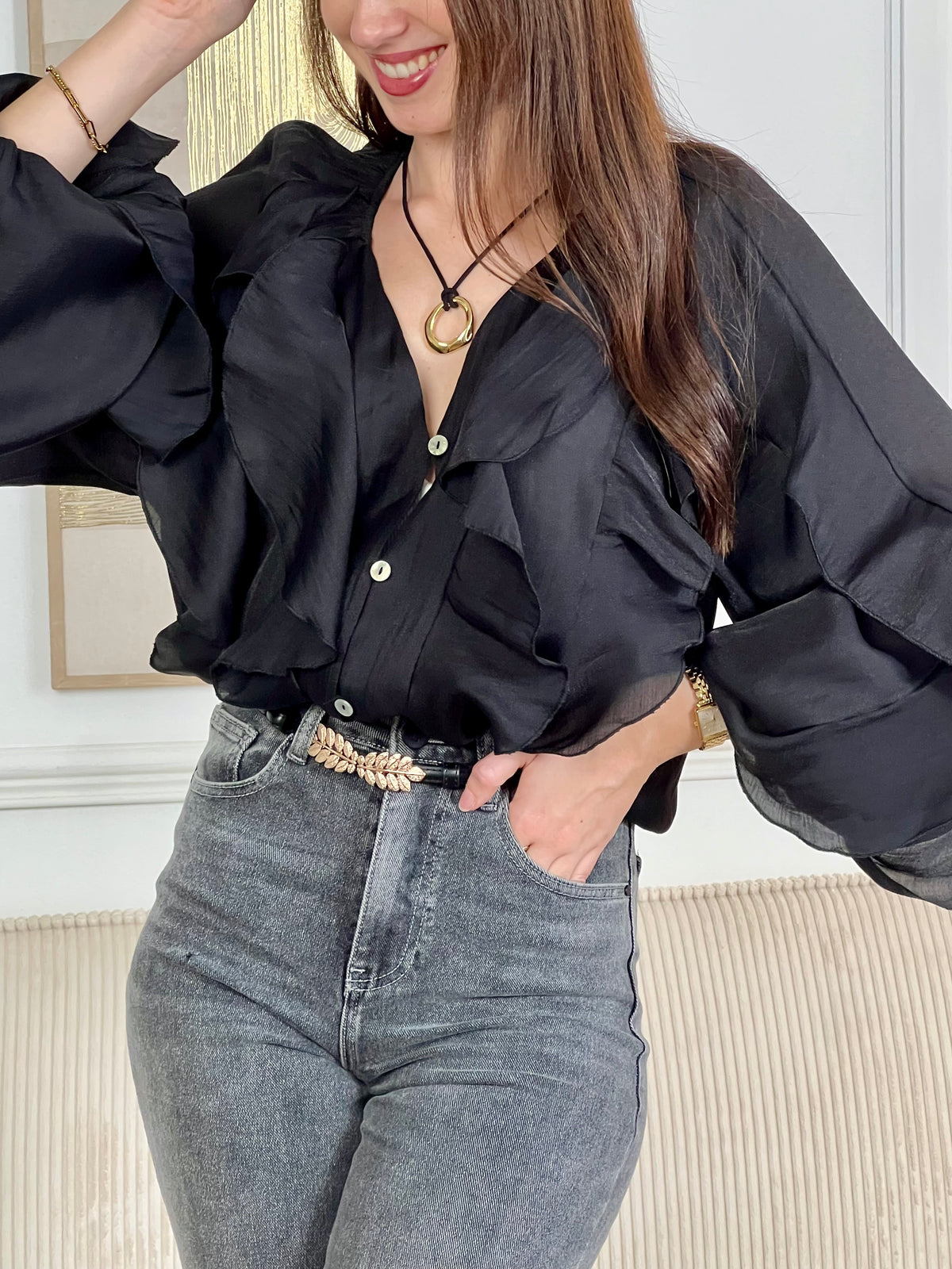 Légère et pleine de charme, cette chemise noire pour femme apporte une touche lumineuse et féminine à votre tenue. Son col V délicatement souligné par un élastique met en valeur le décolleté, tandis que les poignets élastiqués assurent un joli tombé aux manches longues. Les volants au col, aux épaules et aux manches ajoutent du mouvement et une note romantique à l’ensemble. Sa matière légèrement transparente renforce son côté aérien et élégant.