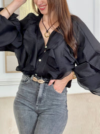 Légère et pleine de charme, cette chemise noire pour femme apporte une touche lumineuse et féminine à votre tenue. Son col V délicatement souligné par un élastique met en valeur le décolleté, tandis que les poignets élastiqués assurent un joli tombé aux manches longues. Les volants au col, aux épaules et aux manches ajoutent du mouvement et une note romantique à l’ensemble. Sa matière légèrement transparente renforce son côté aérien et élégant.