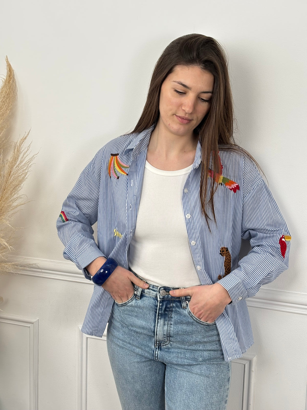 Découvrez Adia, notre chemise en coton pensée pour vous. Avec ses manches longues et son col chemise classique, elle allie élégance et confort. Les rayures verticales bleues et écrues créent une base intemporelle, sublimée par des motifs brodés colorés qui ajoutent du caractère.