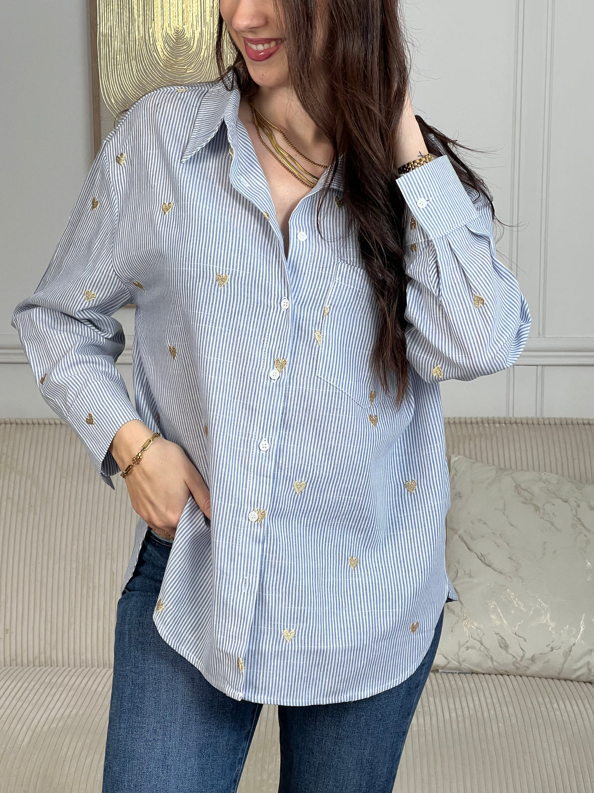 La chemise Sélène en coton combine style intemporel et détails délicats. Rayures verticales bleu et écru, cœurs dorés brodés et col chemise structuré créent une allure sophistiquée. Manches longues avec boutons aux poignets, poche poitrine et fermeture boutonnée complète.