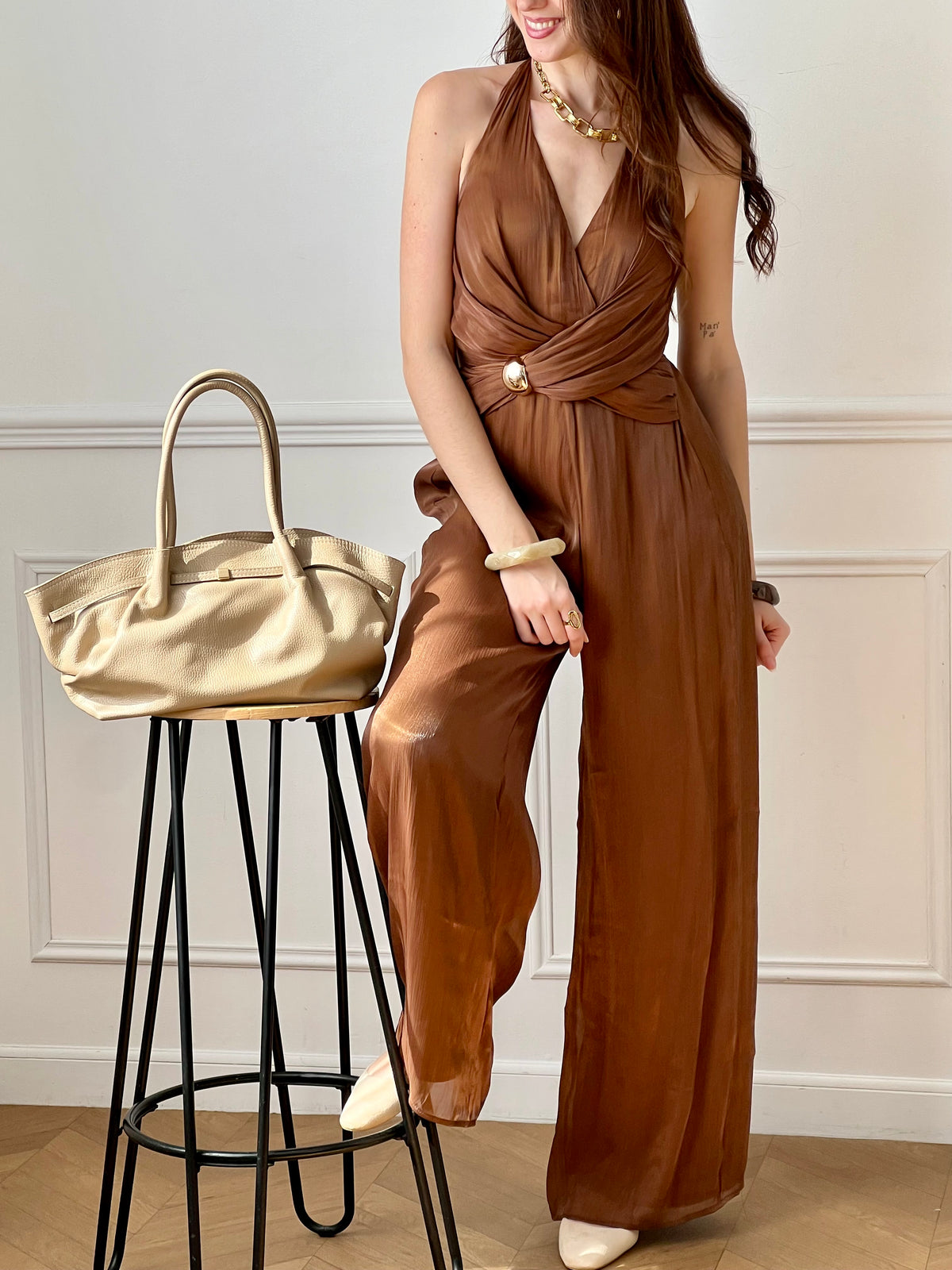 Cette combinaison satinée marron séduit par son élégance et sa fluidité. Son col en V met en valeur le décolleté, tandis que le lien nouable à la nuque apporte une touche féminine et raffinée. Idéale pour un look chic et sophistiqué.