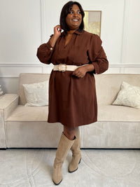 Cette robe courte en marron séduit par sa coupe ample et son col V à revers. Dotée de manches longues, de poches pratiques et de détails dorés aux poignets, elle allie confort et style au quotidien.