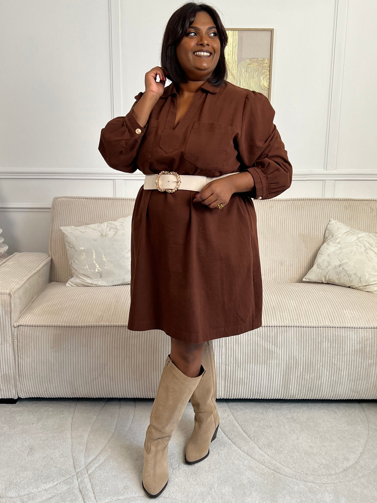 Cette robe courte en marron séduit par sa coupe ample et son col V à revers. Dotée de manches longues, de poches pratiques et de détails dorés aux poignets, elle allie confort et style au quotidien.