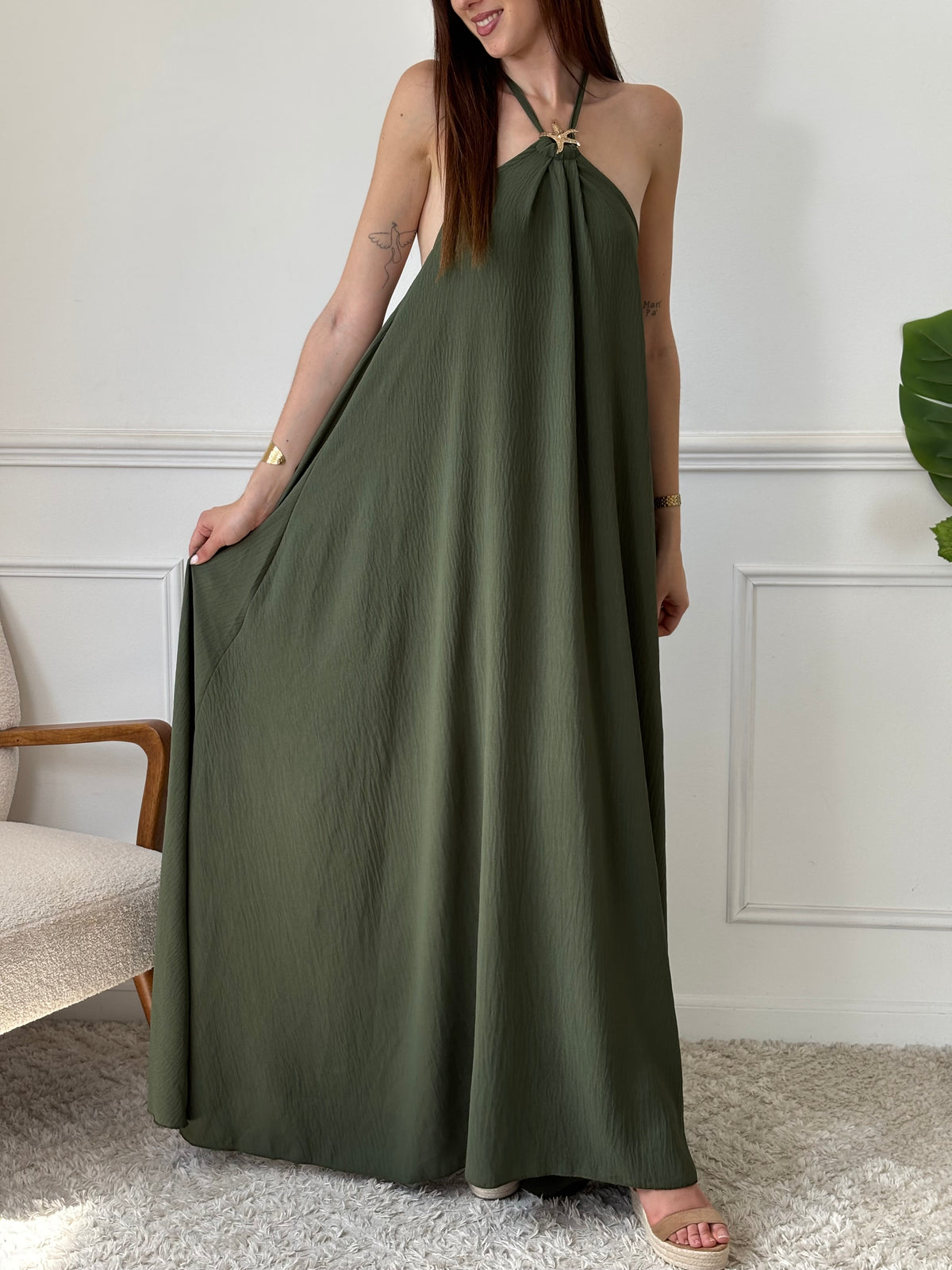Adoptez une allure audacieuse avec cette robe longue kaki Adeje. Son col montant réglable, orné d’un détail doré, apporte une touche sophistiquée tandis que l’élastique au dos assure un confort parfait. Sans manches et à la coupe ample, elle offre une liberté de mouvement idéale pour affirmer votre style avec assurance.&nbsp;