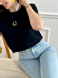 Jean bleu femme coupe straight intemporelle, agrémenté de motifs ananas brodés en jaune et vert pour une touche de couleur ludique. Fermeture à zip et bouton, quatre poches pratiques. Confectionné en coton, ce jean allie confort et style décontracté, parfait pour un look casual chic au quotidien.