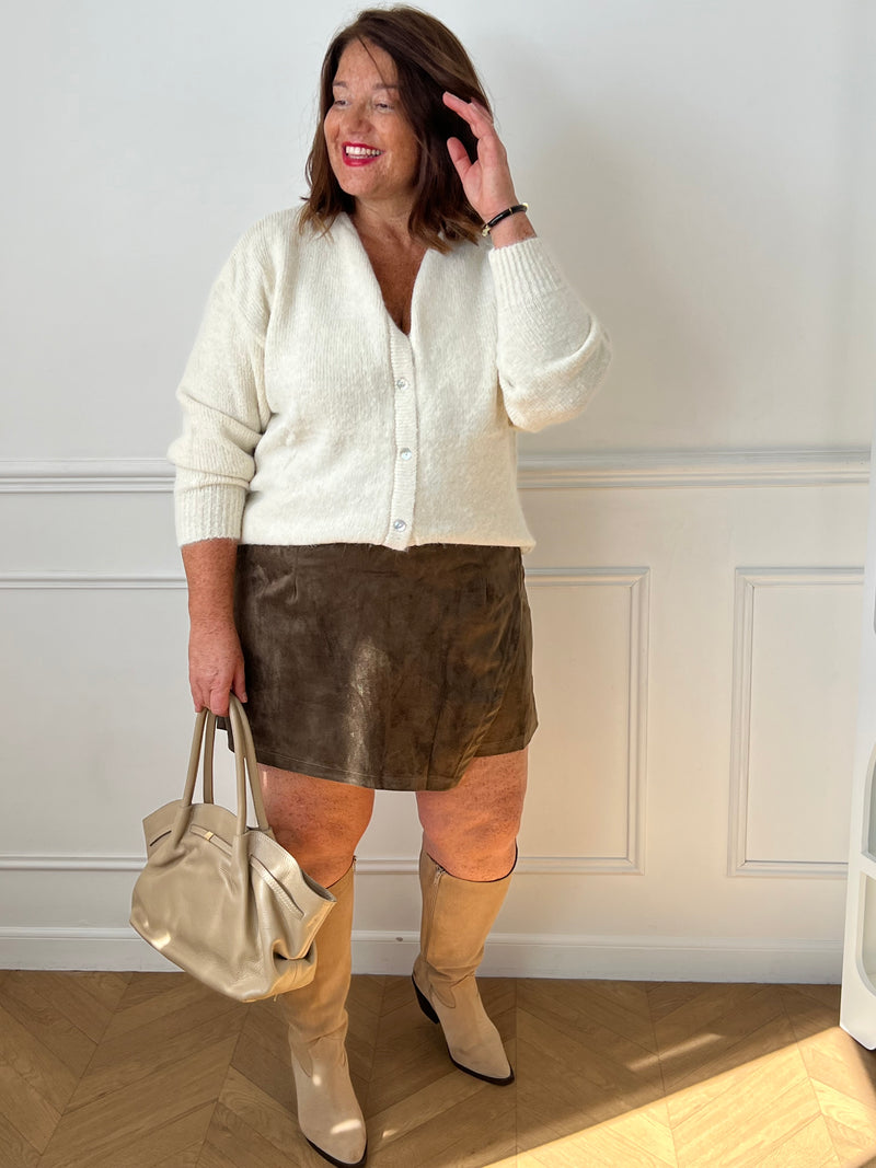  Jupe-short kaki Adele grande taille portée de face avec un gilet écru, des bottes beiges et un sac clair.