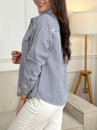 Découvrez la surchemise Anabelle, une pièce incontournable pour un style décontracté et élégant. Confectionnée en coton, elle arbore des rayures verticales subtiles dans les tons écru et bleu. Son col chemise classique et ses manches longues offrent une allure intemporelle, tandis que les motifs brodés délicats sur le devant et les manches ajoutent une touche de caractère.