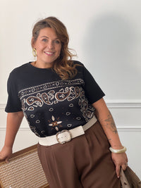 Vue rapprochée du tee-shirt noir Livana à motifs cachemire écrus et marron, porté rentré dans un pantalon marron avec une ceinture écrue.