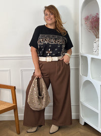 Tee-shirt noir Livana grande taille porté de face avec un pantalon large marron, une ceinture écrue et un sac taupe à clous.