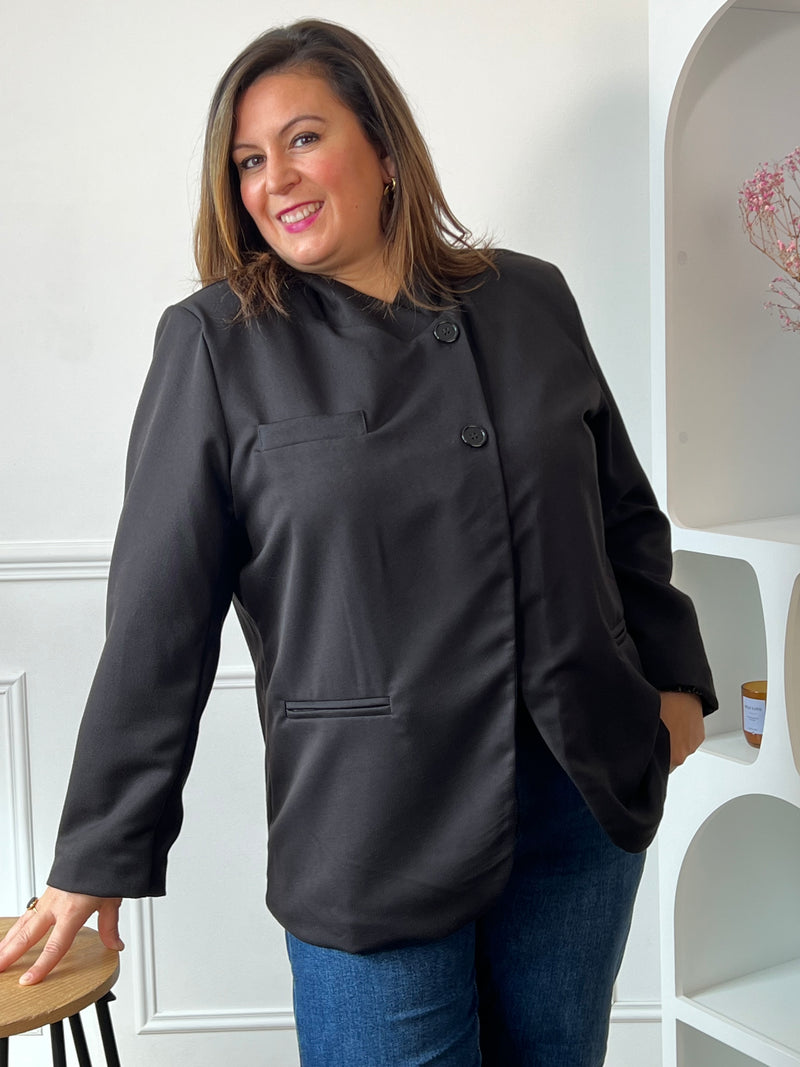 Veste noire Loen portée boutonnée avec un jean bleu, montrant les poches passepoilées et les pans arrondis.