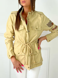 VESTE SAHARIENNE FEMME BEIGE AJUSTABLE A LA TAILLE Veste manches longues Boutons sur la longueur et aux poignets Fermeture éclair 4 poches à l’avant Eléments décoratifs sur la manche gauche Couleur : beige Cordon ajustable à la taille Longueur env 60 cm en taille XS Composition : 100% Coton