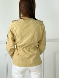 VESTE SAHARIENNE FEMME BEIGE AJUSTABLE A LA TAILLE Veste manches longues Boutons sur la longueur et aux poignets Fermeture éclair 4 poches à l’avant Eléments décoratifs sur la manche gauche Couleur : beige Cordon ajustable à la taille Longueur env 60 cm en taille XS Composition : 100% Coton