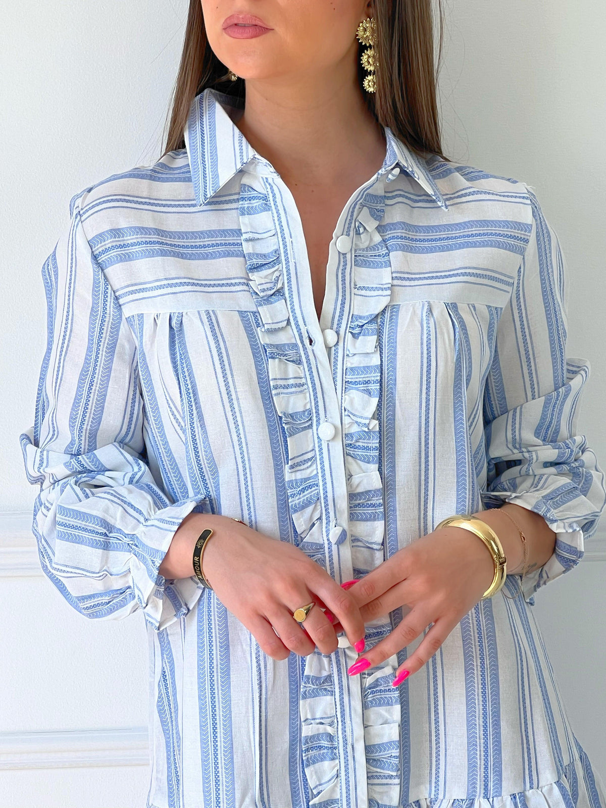 ROBE BLEUE ET BLANCHE À VOLANTS Robe chemise Volants et boutons sur la longueur Col chemise Elastiquée aux poignets Coupe ample Motif rayure écrue et grise Couleurs : bleu et ecru Composition : 60% Coton 30% Viscose Lavage à la main
