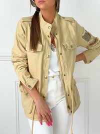 VESTE SAHARIENNE FEMME BEIGE AJUSTABLE A LA TAILLE Veste manches longues Boutons sur la longueur et aux poignets Fermeture éclair 4 poches à l’avant Eléments décoratifs sur la manche gauche Couleur : beige Cordon ajustable à la taille Longueur env 60 cm en taille XS Composition : 100% Coton