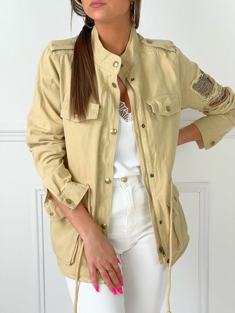 VESTE SAHARIENNE FEMME BEIGE AJUSTABLE A LA TAILLE Veste manches longues Boutons sur la longueur et aux poignets Fermeture éclair 4 poches à l’avant Eléments décoratifs sur la manche gauche Couleur : beige Cordon ajustable à la taille Longueur env 60 cm en taille XS Composition : 100% Coton