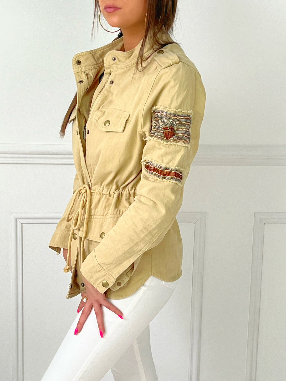 VESTE SAHARIENNE FEMME BEIGE AJUSTABLE A LA TAILLE Veste manches longues Boutons sur la longueur et aux poignets Fermeture éclair 4 poches à l’avant Eléments décoratifs sur la manche gauche Couleur : beige Cordon ajustable à la taille Longueur env 60 cm en taille XS Composition : 100% Coton