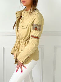 VESTE SAHARIENNE FEMME BEIGE AJUSTABLE A LA TAILLE Veste manches longues Boutons sur la longueur et aux poignets Fermeture éclair 4 poches à l’avant Eléments décoratifs sur la manche gauche Couleur : beige Cordon ajustable à la taille Longueur env 60 cm en taille XS Composition : 100% Coton